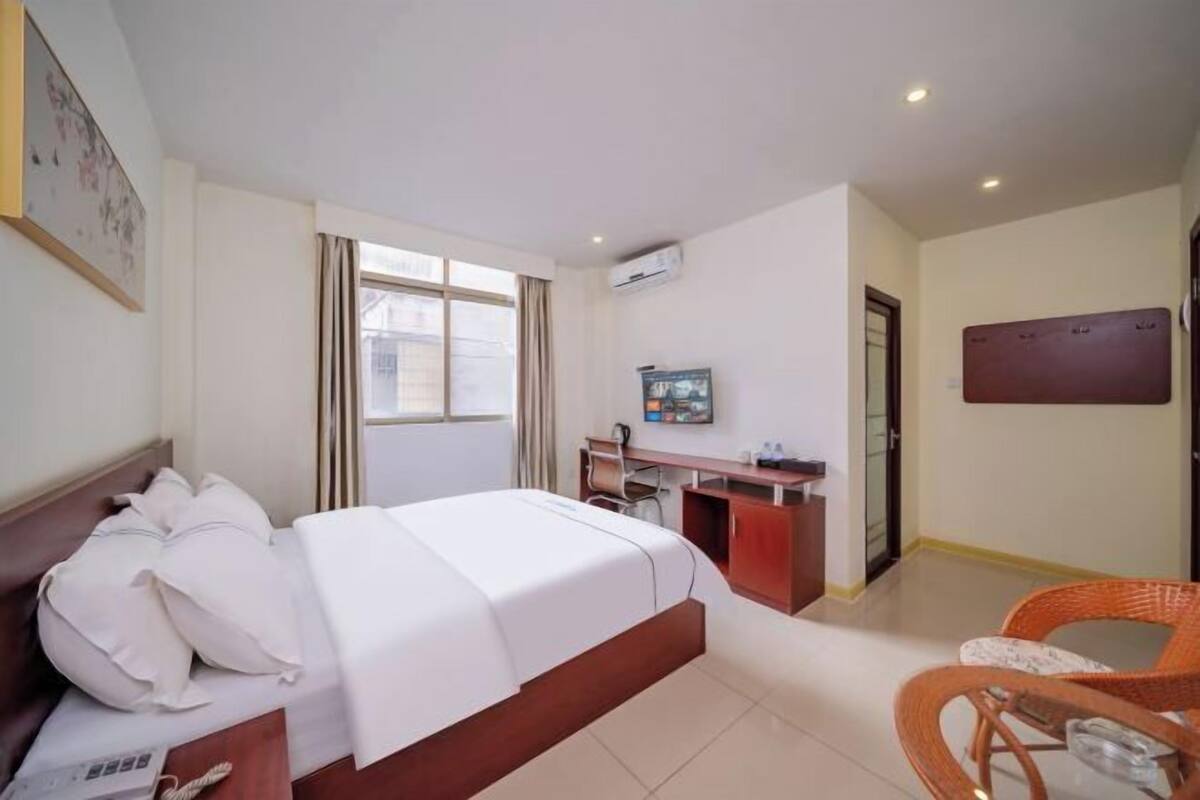 Quarto de hotel com cama, escrivaninha, cadeira e televisão.