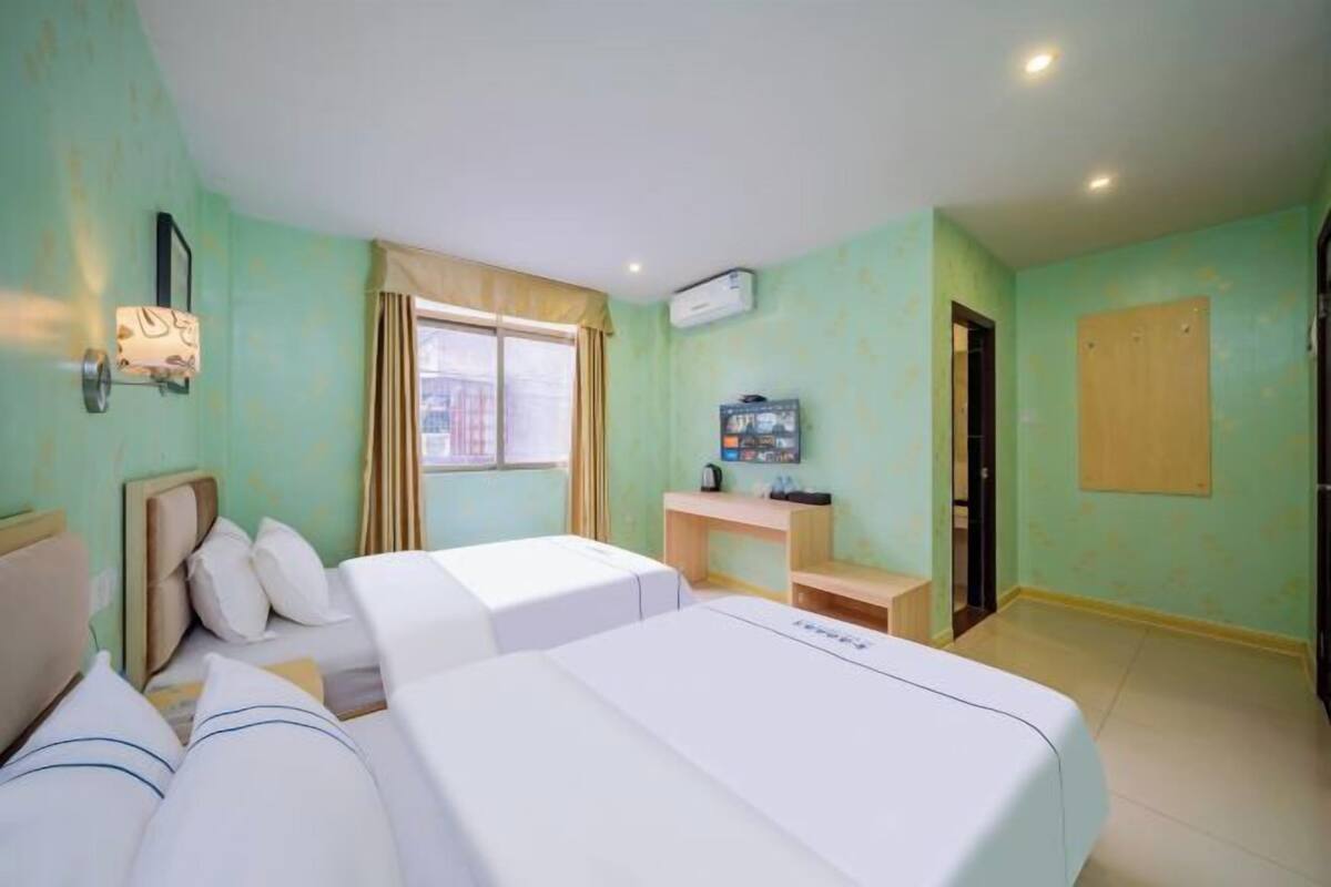 Quarto de hotel com duas camas, televisão, escrivaninha e janela.