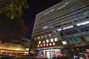 A multi-story building with illuminated signage, a parking lot, and a tree in the foreground. - Yingzhou Business Hotel (Zhuhai)