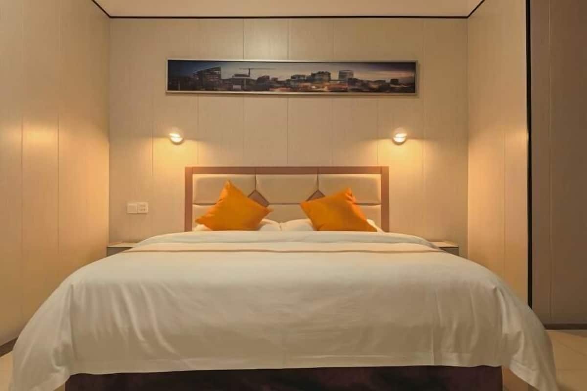 A hotel room with a bed, a headboard, and a cityscape painting above the bed.