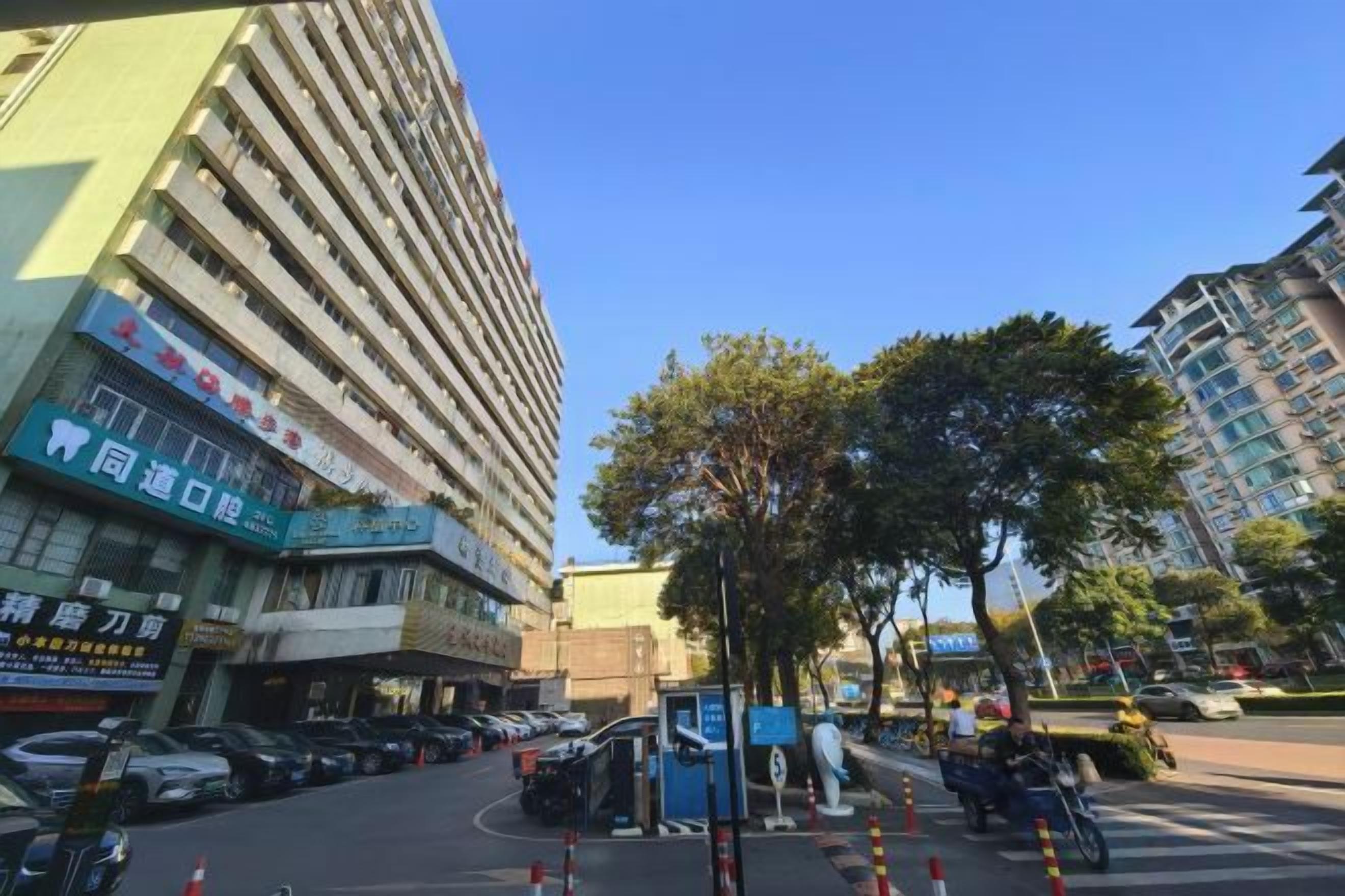 A multi-story building with commercial signage, a parking area, and a tree-lined street.