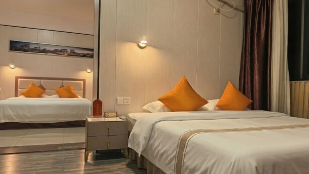 A hotel room with two beds, each with white bedding and orange pillows, a nightstand with a lamp, and a large mirror on the wall. - Yingzhou Business Hotel (Zhuhai)