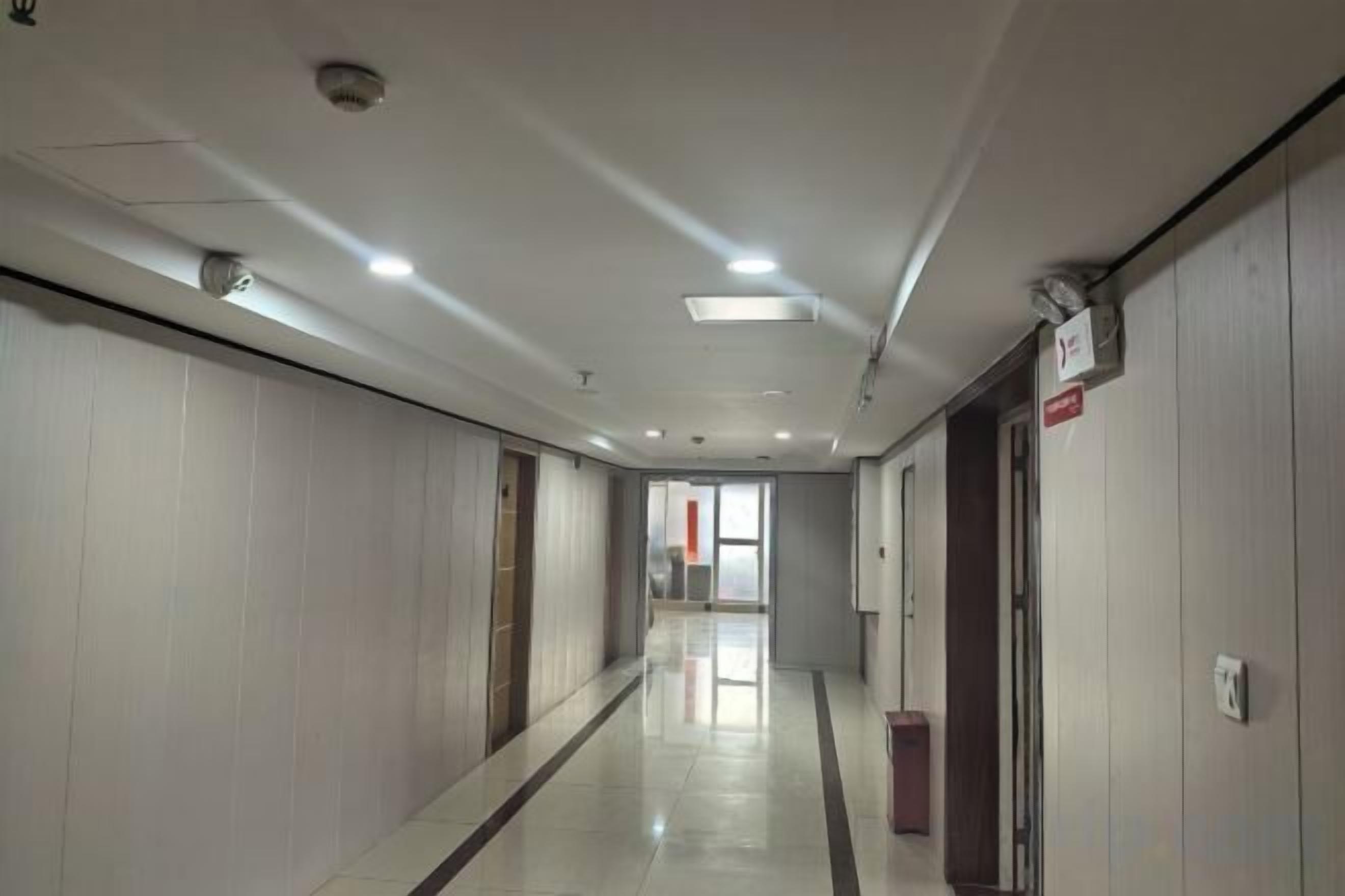 Un pasillo con puertas a ambos lados, piso de baldosas y luces en el techo.
