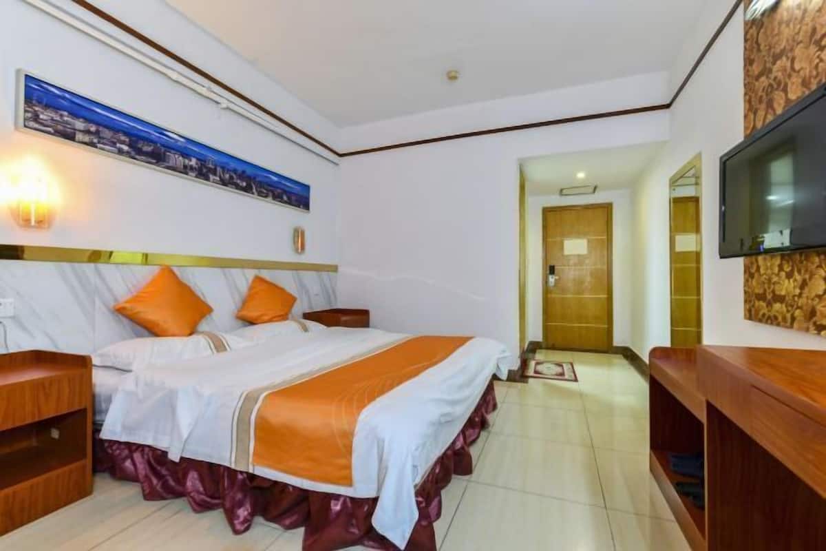 A hotel room with a large bed, two nightstands, a TV mounted on the wall, and a wooden door leading to another room.