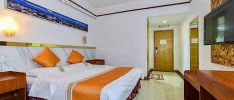 Ein Hotelzimmer mit einem großen Bett, zwei Nachttischen, einem an der Wand montierten Fernseher und einer Holztür, die in einen anderen Raum führt.