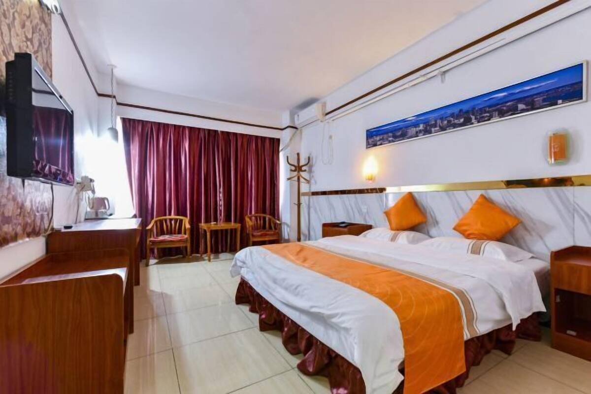 A hotel room with a large bed, a desk, a chair, and a television.