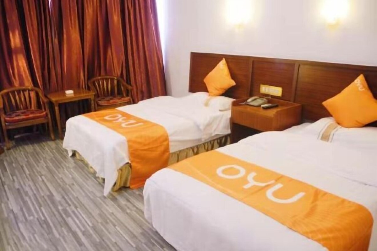 A hotel room with two beds, each with a white bedspread and orange accents, wooden headboards, and a small table with a chair.