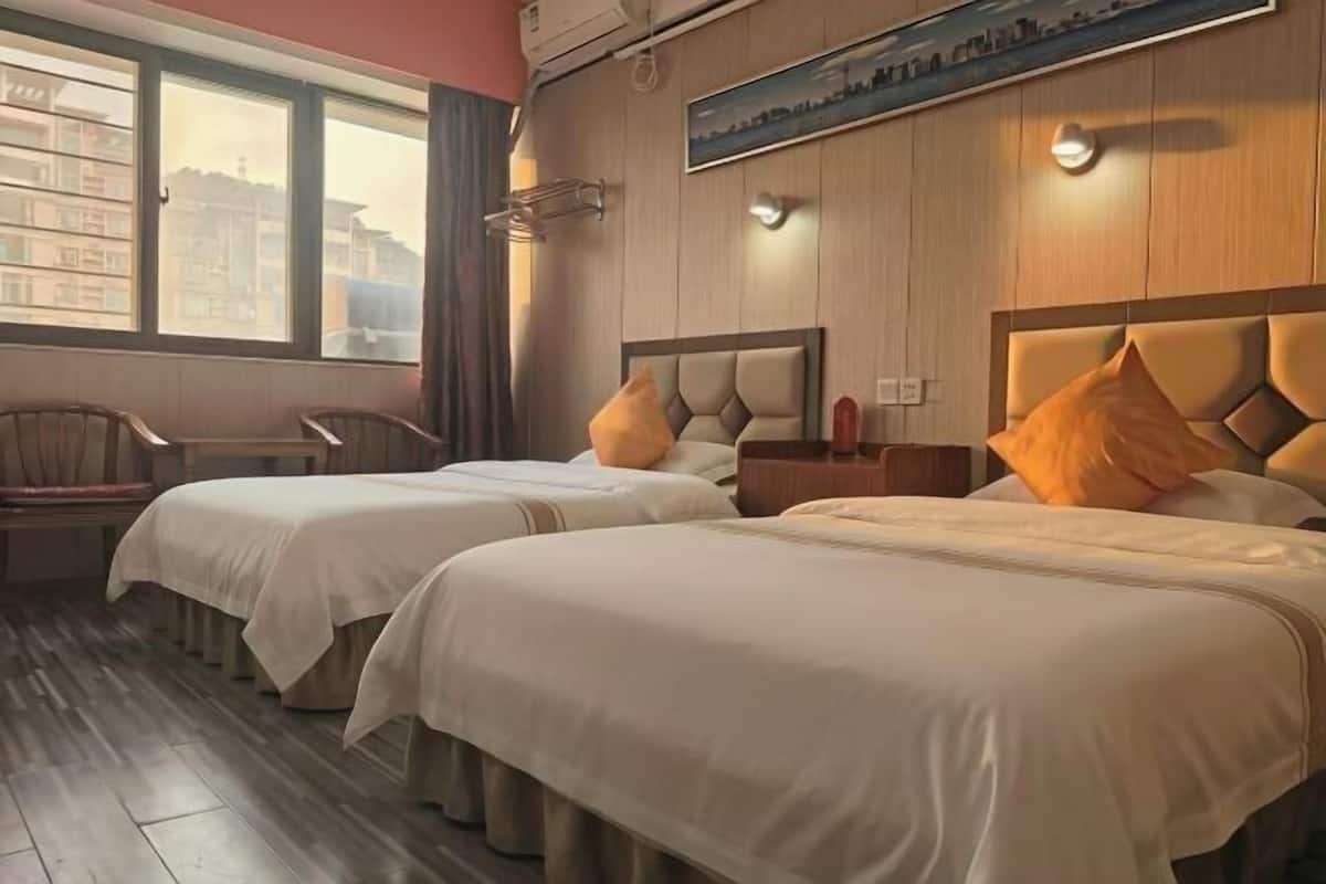A hotel room with two beds, a chair, a nightstand, and a large window.