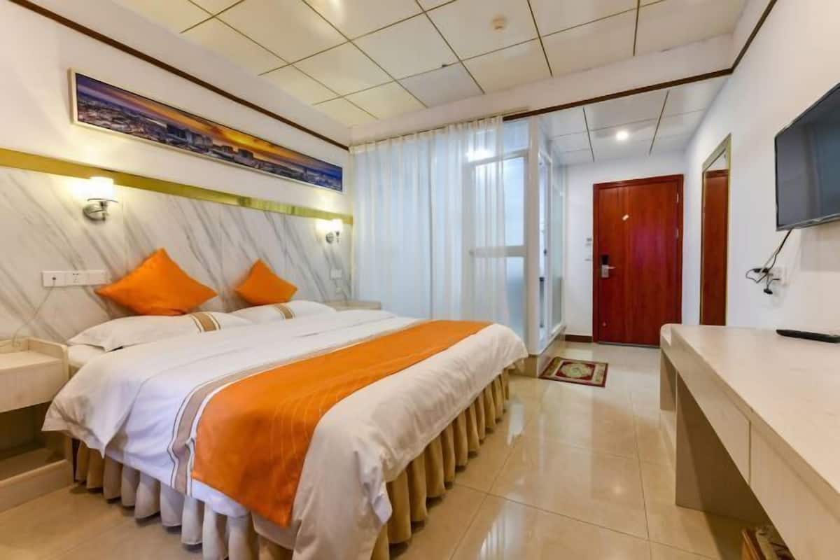 A hotel room with a bed, a bedside table, a TV, and a door.