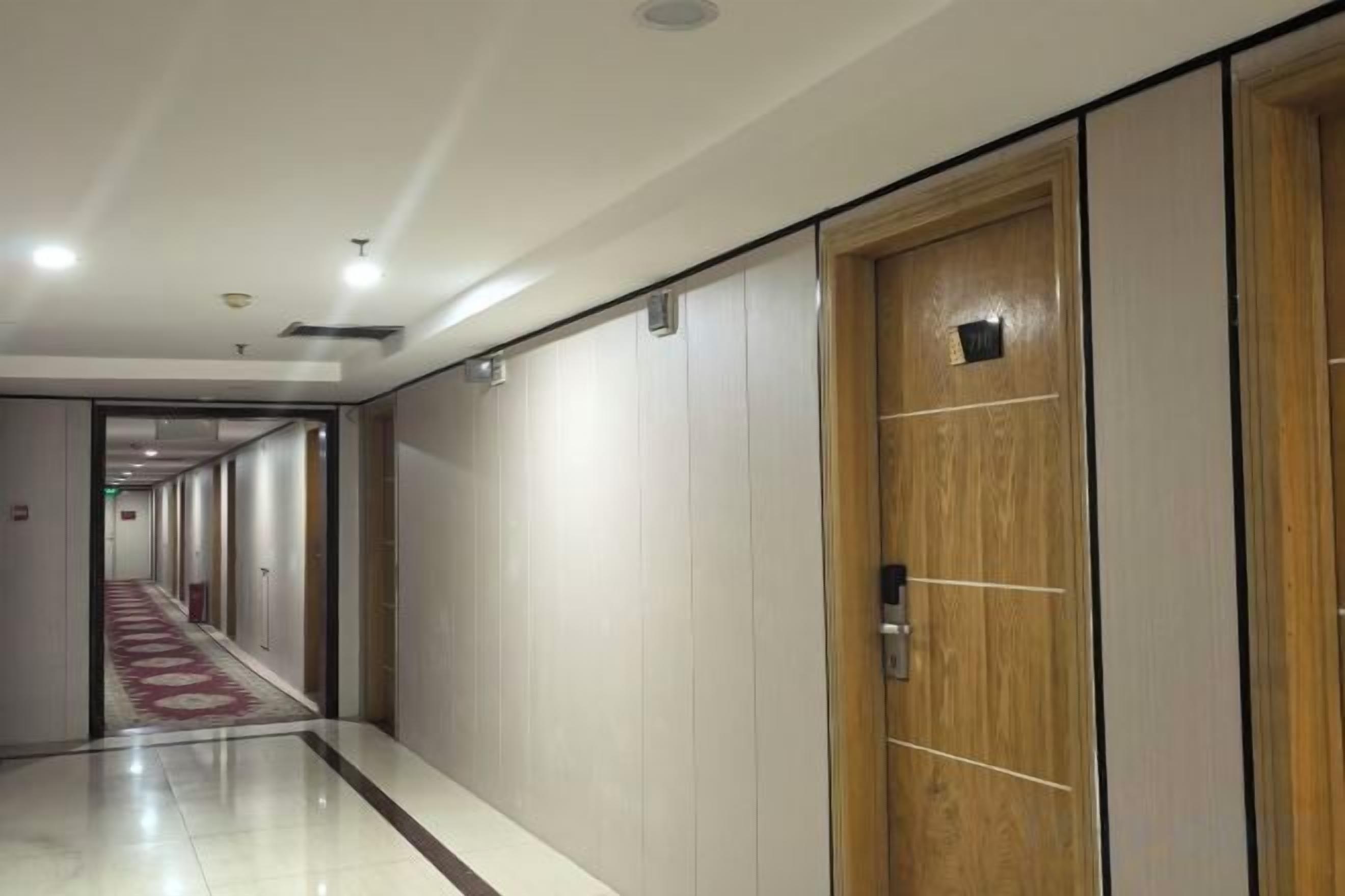 A hotel corridor with a wooden door, a red carpet, and a long hallway with doors on both sides.