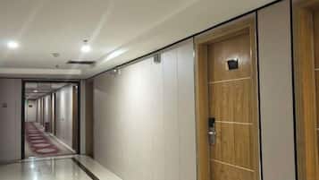 A hotel corridor with a wooden door, a red carpet, and a long hallway with doors on both sides.