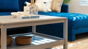 A modern living room with a blue sofa, a coffee table with a book titled "SURF-HAU", a candle, and two woven baskets. - Casa Coco: Private Designer Home Pool / Close to Brickell & Coconut Grove (Miami)