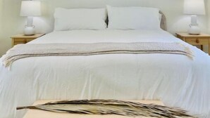 Ein Schlafzimmer mit einem Bett, das zwischen zwei Nachttischen platziert ist, von denen jeder eine Lampe trägt. Eine besondere Deckenleuchte strahlt Licht aus der Mitte aus.
