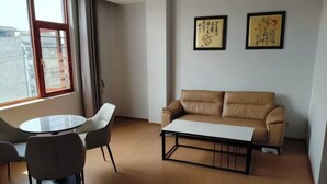 A room with a brown leather sofa, a round table, and two chairs. There are two framed artworks on the wall. - Mouding Minghuang Hotel (Mouding)