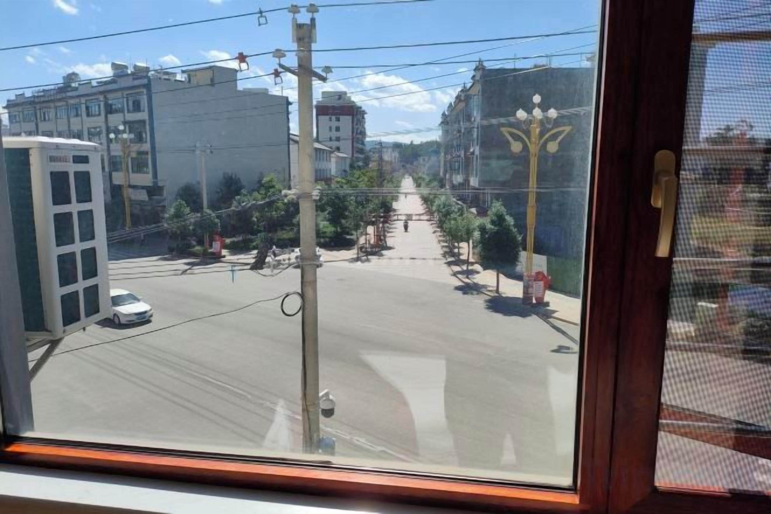 Vista de la calle desde una ventana, con edificios, cielo despejado y un automóvil estacionado.