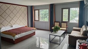 A hotel room with a bed, a sofa, a coffee table, and a window with a view of greenery. - Mouding Minghuang Hotel (Mouding)