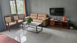 A living room with a beige sofa, a small coffee table, a TV, and a window with curtains. - Mouding Minghuang Hotel (Mouding)