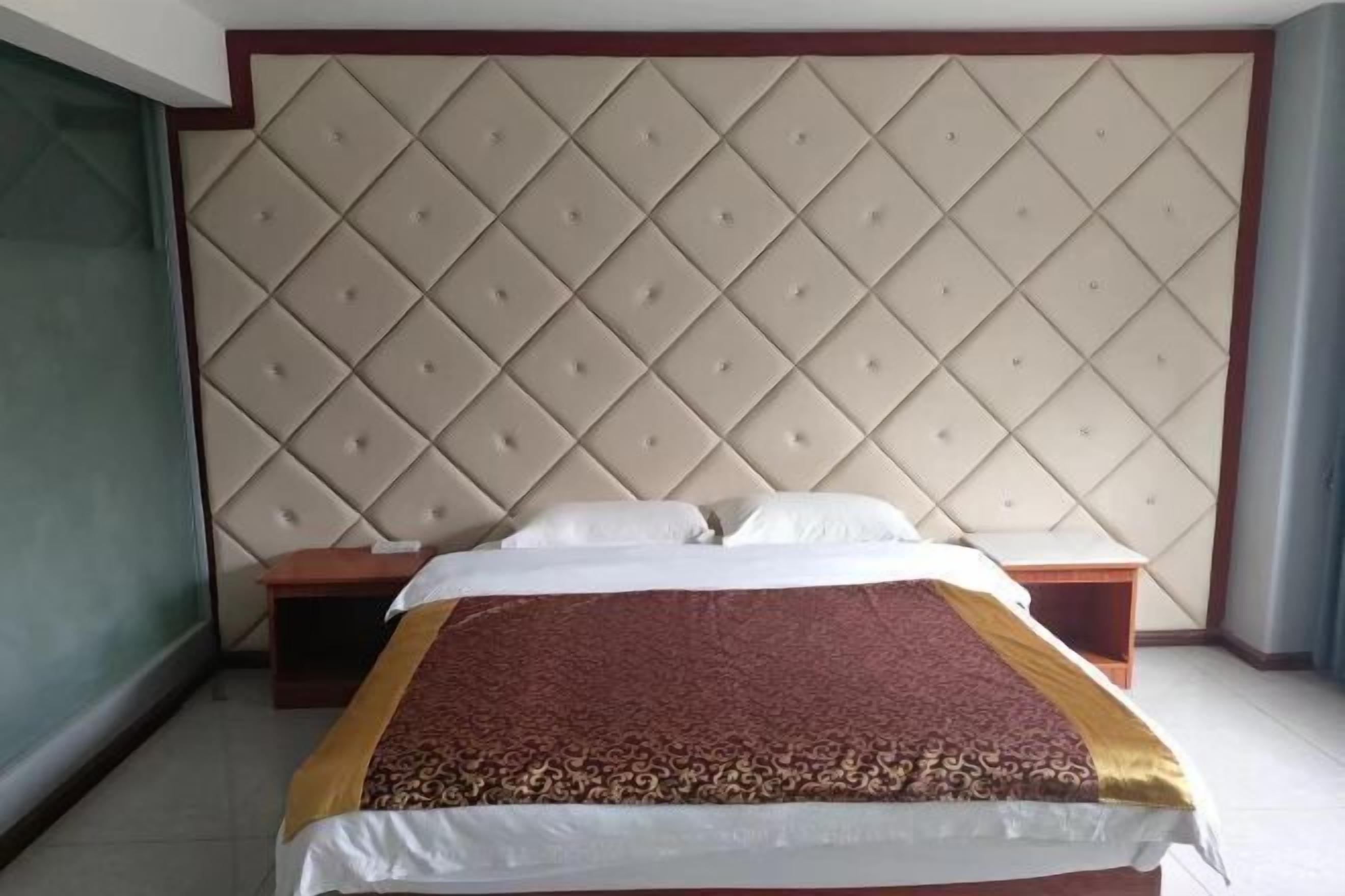A hotel room with a large bed, a padded headboard, and a small bedside table.