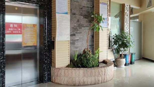 A hotel lobby with a reception desk, a glass elevator, and a plant arrangement. - Mouding Minghuang Hotel (Mouding)