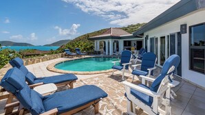 A pool area with lounge chairs and a view of the sea.