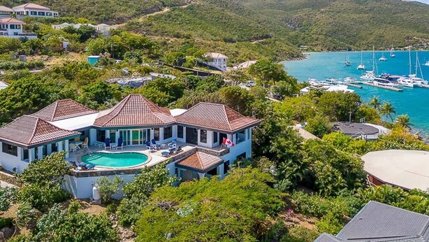 A large house with a swimming pool, surrounded by lush greenery and a marina with boats.