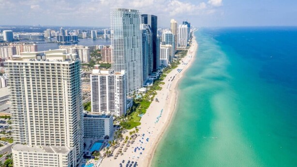 Un paisaje urbano costero con rascacielos, una playa y un mar azul cristalino.