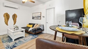 Una sala de estar moderna con un sofá, una mesa de comedor preparada para dos personas y un ventilador de techo.