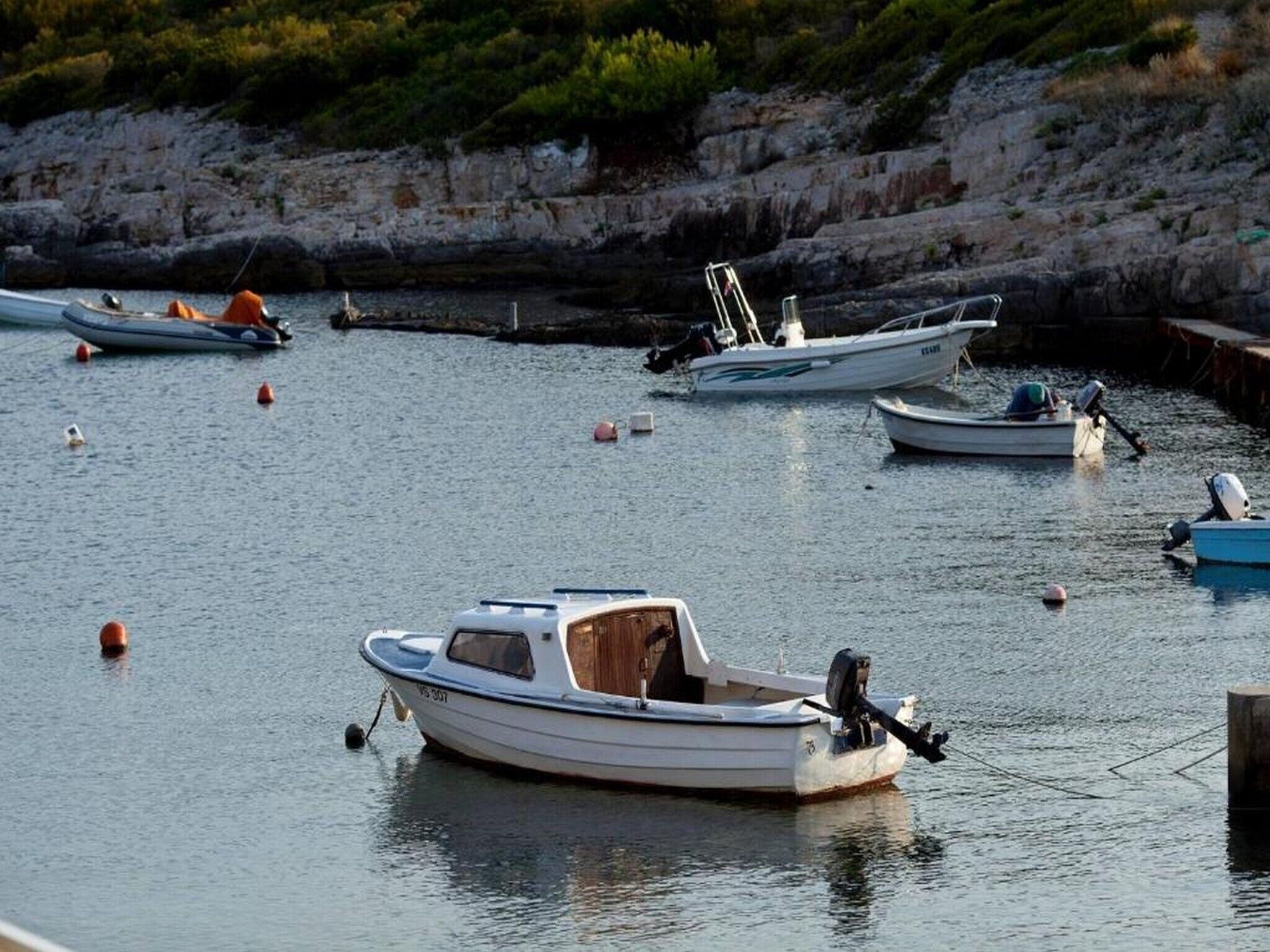 A marina with several small boats anchored in calm waters, surrounded by rocky cliffs and sparse vegetation.