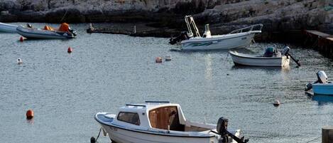 A marina with several small boats anchored in calm waters, surrounded by rocky cliffs and sparse vegetation.
