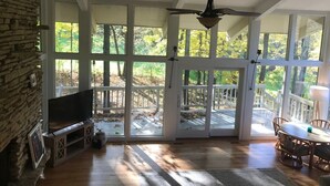 Une pièce spacieuse avec un mur en pierre, un téléviseur à écran plat, un ventilateur de plafond et une grande porte-fenêtre coulissante donnant sur une terrasse extérieure.