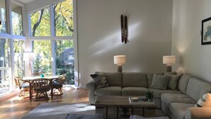 Un salon moderne doté d’une grande fenêtre, d’un canapé, d’une table basse et d’un coin repas avec des chaises.