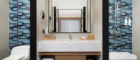 Une salle de bain moderne avec un lavabo blanc, un miroir et une douche équipée d’un pommeau de douche à main.