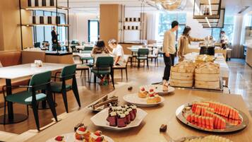 Een modern café met diverse gerechten gepresenteerd op tafels, waaronder fruit, gebak en belegde broodjes.