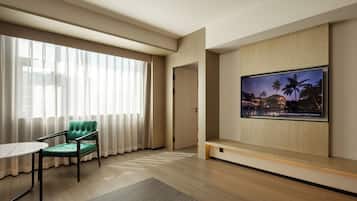 Una habitación de hotel moderna con un ventanal grande, un sillón tapizado en verde, un televisor de pantalla plana montado en la pared y suelo de madera.
