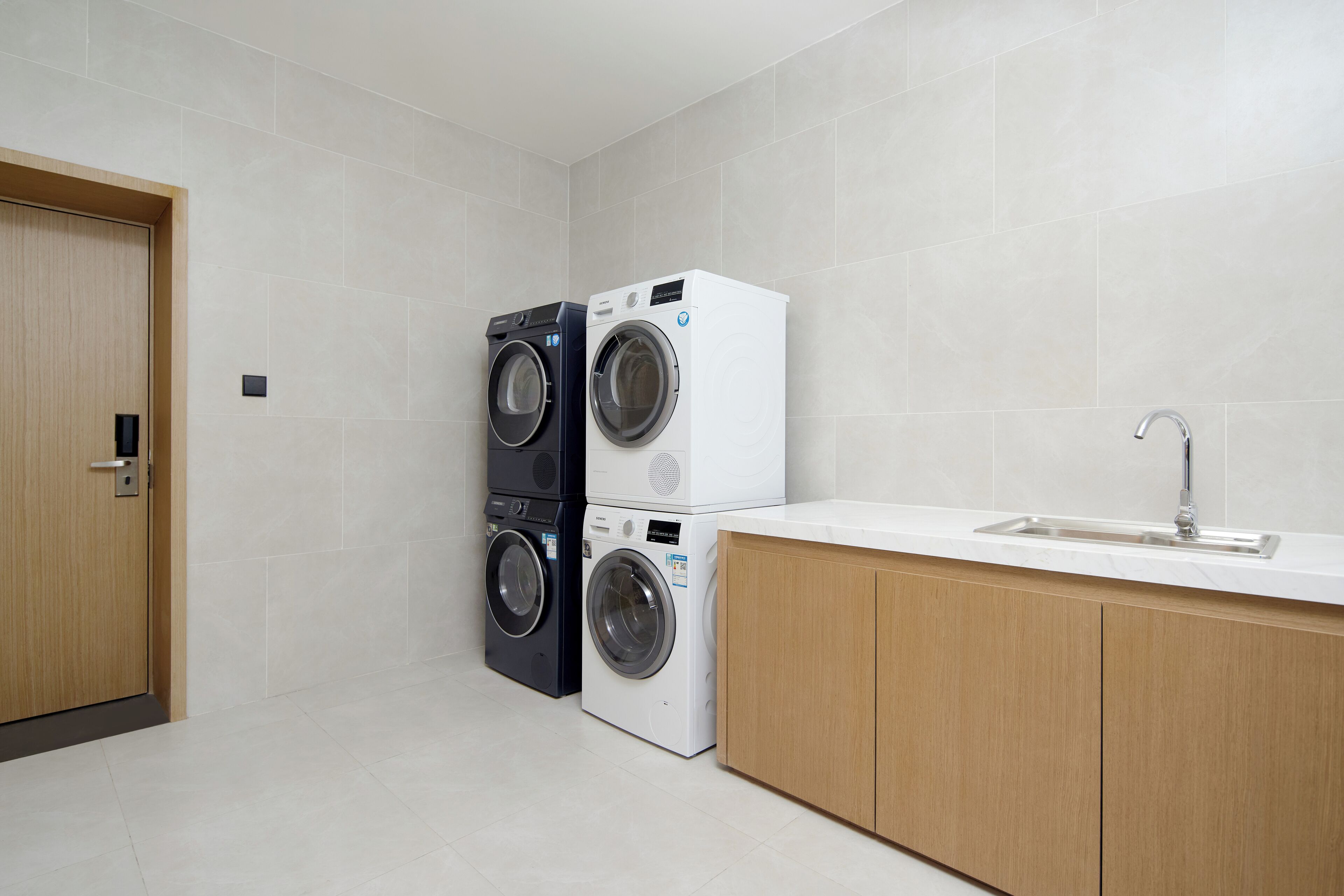 A laundry room with two stacked washing machines, a sink, and wooden cabinetry.