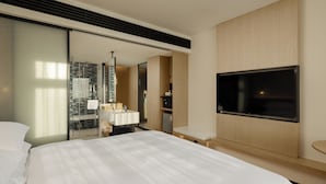 A modern hotel room with a large bed, a flat-screen TV mounted on the wall, a glass shower enclosure, and a wooden vanity with a mirror. - Fairfield by Marriott Lijiang Ancient Town (Lijiang)