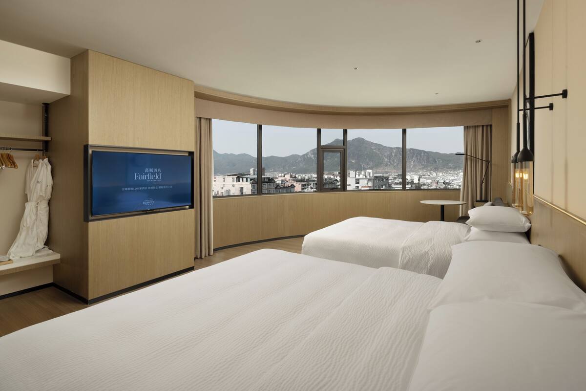Une chambre d’hôtel avec deux lits, un téléviseur fixé au mur et une vue sur le paysage urbain.