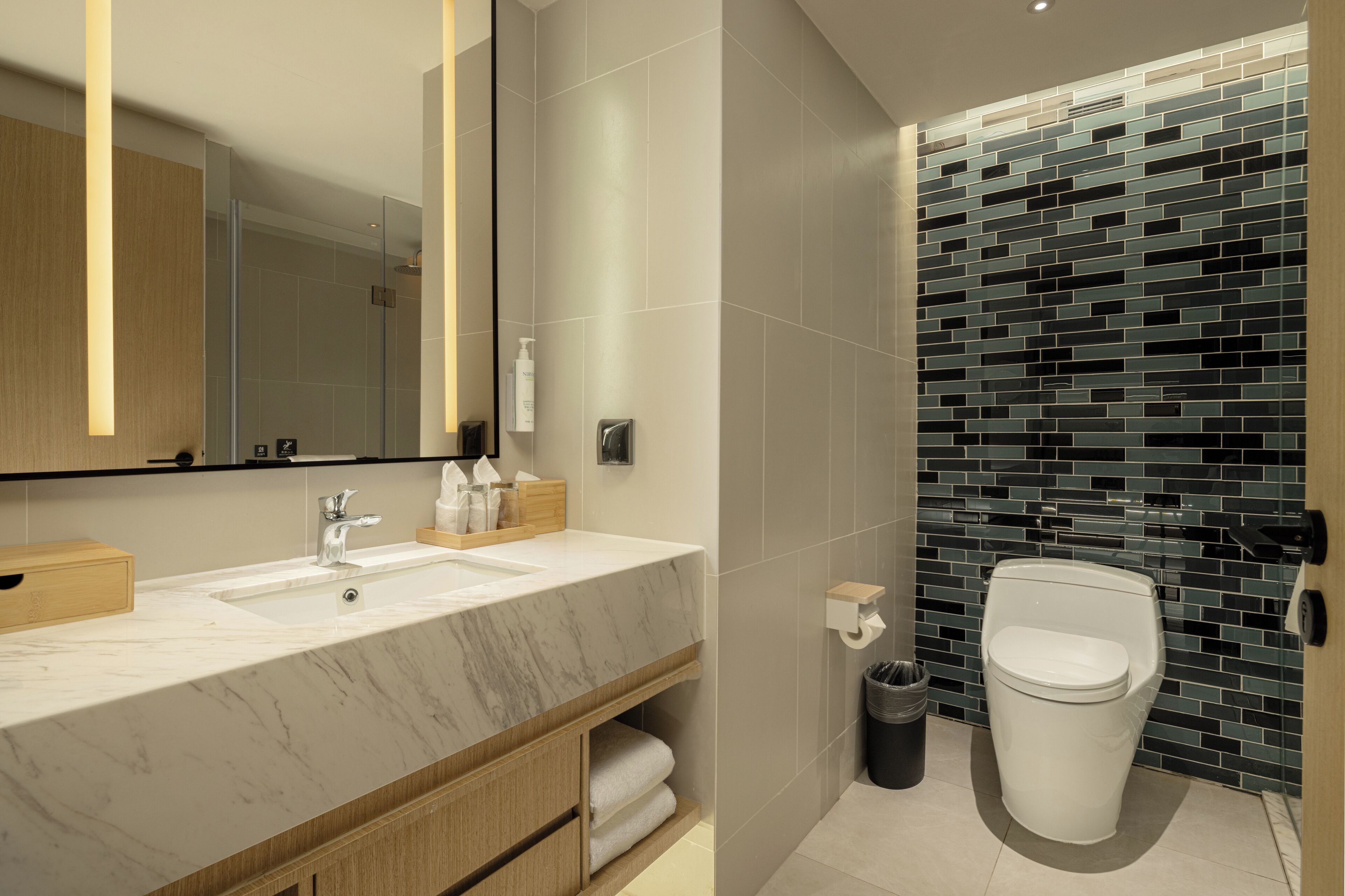 Et moderne badeværelse med vask i marmor, et stort spejl og et toilet med væg i mosaikfliser.