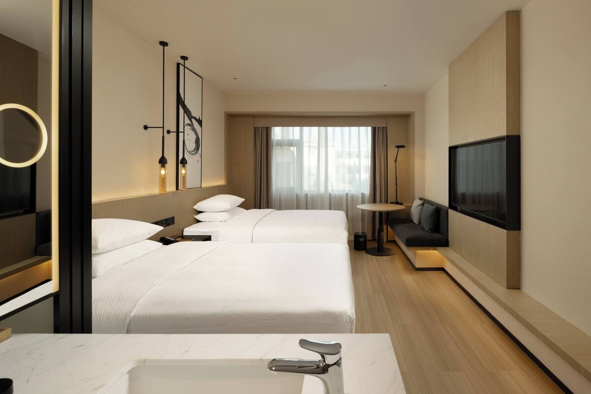 Une chambre d’hôtel avec deux lits, un grand miroir, une télévision et une salle de bain moderne.