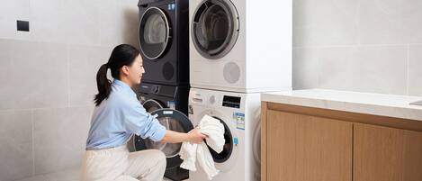 A person kneeling next to a stacked washer and dryer unit in a modern laundry room with a wooden cabinet and a countertop.