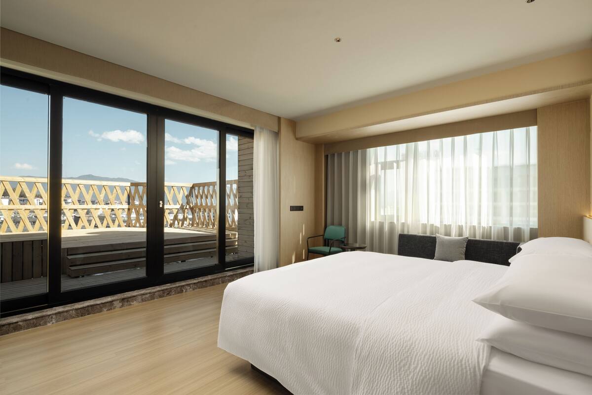 Une chambre d’hôtel avec un grand lit, une vue sur l’extérieur grâce à une porte coulissante et un balcon doté d’une rambarde en bois.