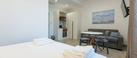 A modern hotel room with a neatly made bed, a dining area with a table and chairs, a sofa, and a painting on the wall.