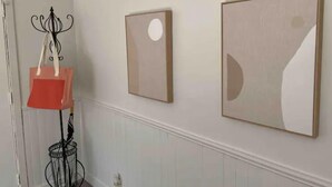 A hallway with white wainscoting, a red floor lamp, and two framed artworks on the wall.