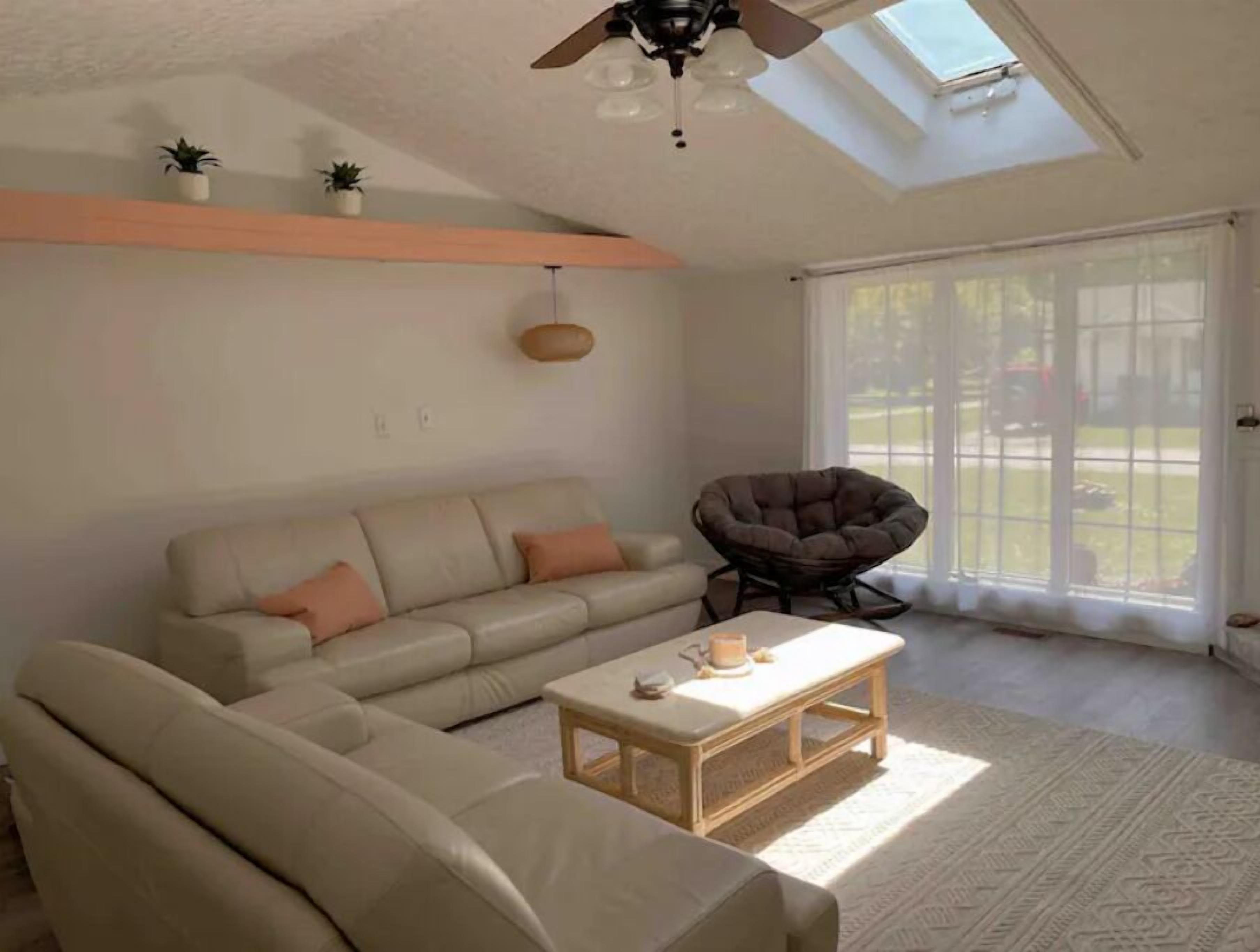 A living room with a sofa, a chair, a coffee table, a ceiling fan, and a skylight.