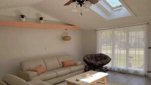 A living room with a sofa, a chair, a coffee table, a ceiling fan, and a skylight.