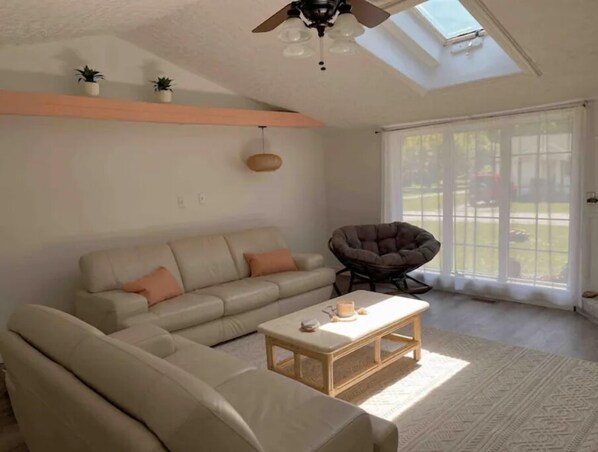 Ein Wohnzimmer mit einer Couch, einem Sessel, einem Couchtisch, einem Deckenventilator und einem Oberlicht.