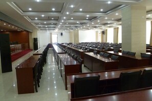 Una sala de conferències amb files de taules i cadires, un escenari al davant i un sostre alt amb il·luminació empotrada.