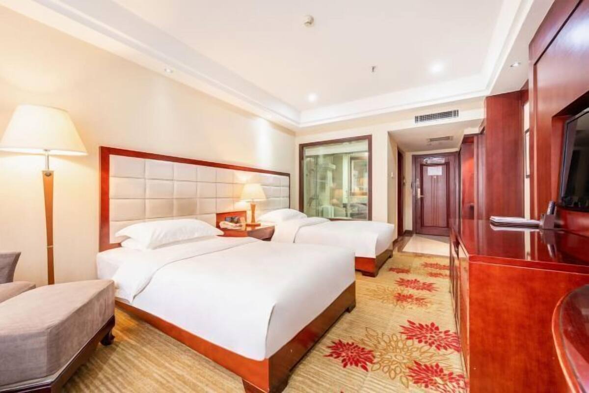 A hotel room with two beds, a TV, a lamp, and a carpeted floor.