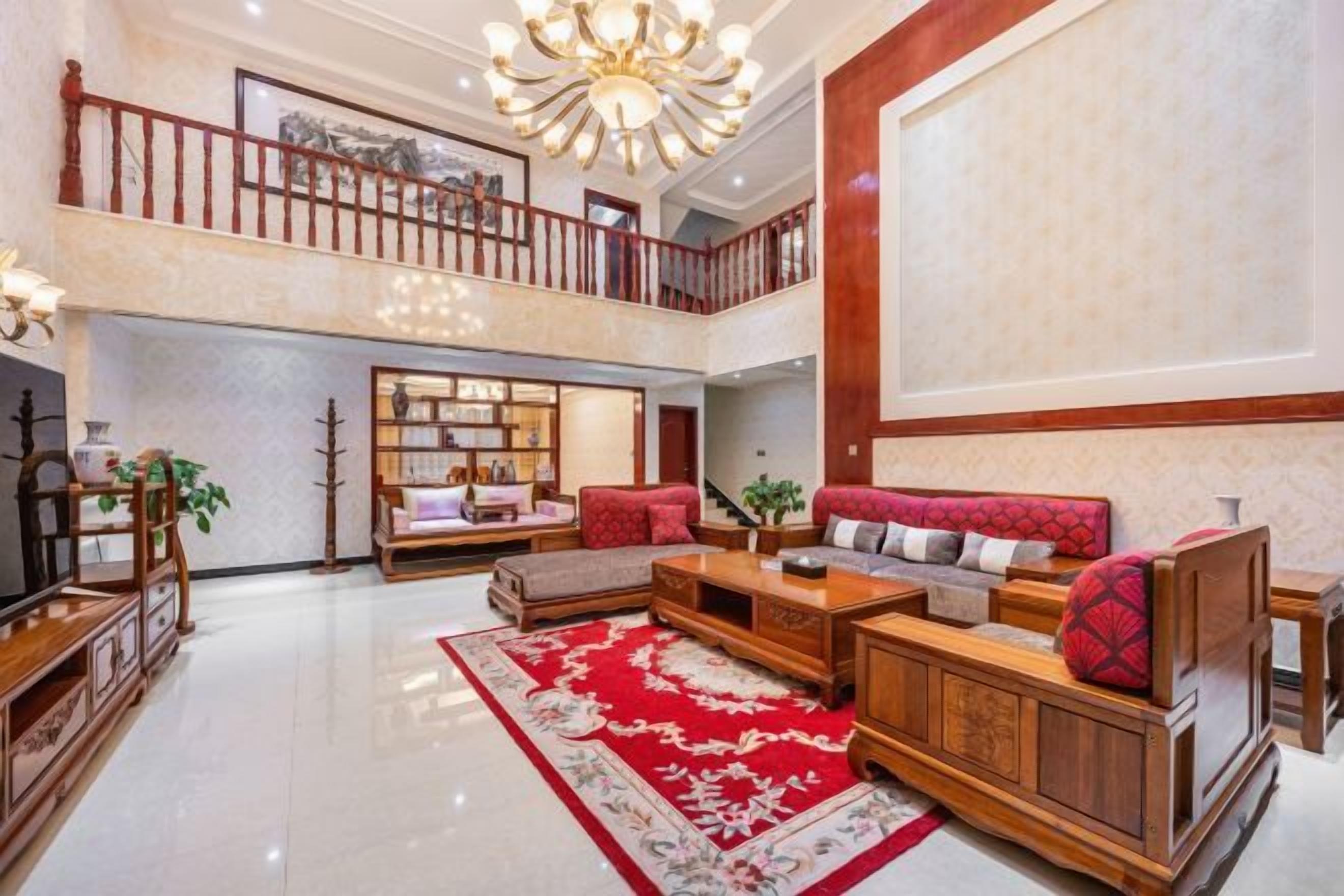 A spacious living area with a high ceiling, a red patterned rug, and a wooden sofa set.