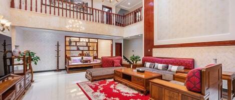 A spacious living area with a high ceiling, a red patterned rug, and a wooden sofa set.